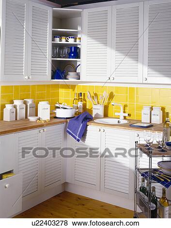 White ceramic storage jars on worktop of economy kitchen with yellow wall tiles and cupboards with white louvre doors View Large Photo Image Stock Photo - White ceramic storage jars on worktop of economy kitchen with yellow wall tiles and cupboards with white louvre doors. Fotosearch
