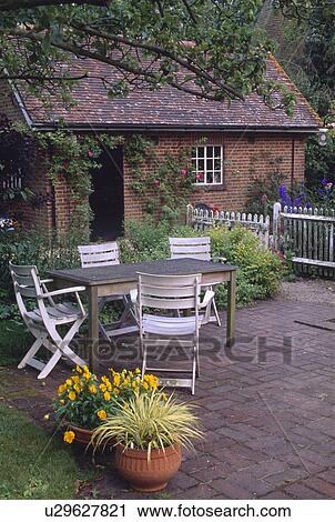 White chairs and old wooden table on paved patio with yellow violas and grasses in pots in summer garden View Large Photo Image Stock Image - White chairs and old wooden table on paved patio with yellow violas and grasses in pots in summer garden. Fotosearch