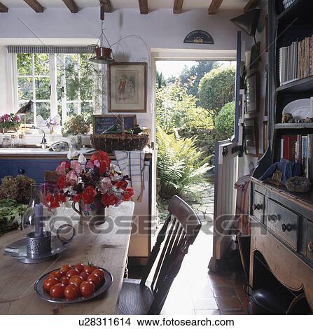 White cottage kitchen with flowers on the table and door open to the garden View Large Photo Image Picture - White cottage kitchen with flowers on the table and door open to the garden. Fotosearch
