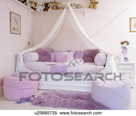 Stock Photography - White drapes above bed with mauve linen and cushions in pink teenage bedroom with mauve and pink beanbags. Fotosearch