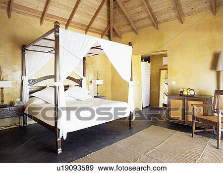Stock Photo - White drapes on bed in yellow Caribbean bedroom. Fotosearch