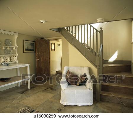 White loose-cover on armchair beside wooden stairs in cottage hall View Large Photo Image Stock Photo - White loose-cover on armchair beside wooden stairs in cottage hall. Fotosearch