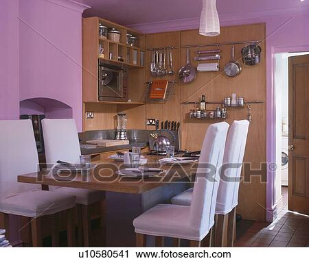 White Loosecovers On Chairs At Wood Table In Modern Mauve Kitchen Dining Room With Utensils And Shelves Wall1010 White Loosecovers On Chairs At Wood Table In Modern Mauve Kitchen Dining Room With Utensils And Shelves Wall1010