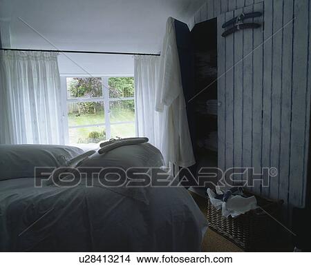 Picture - White pillows and bedlinen on bed in cottage bedroom with fitted wardrobe. Fotosearch