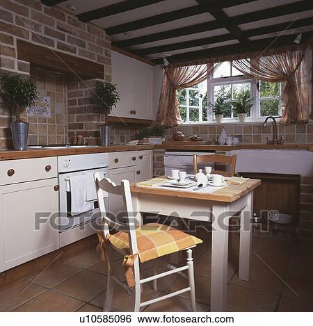 White table and chair in cottage kitchen with fitted white units View Large Photo Image Stock Photograph - White table and chair in cottage kitchen with fitted white units. Fotosearch