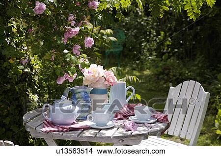 Picture - White table and chairs in grassy corner of rough mown lawn.. Fotosearch