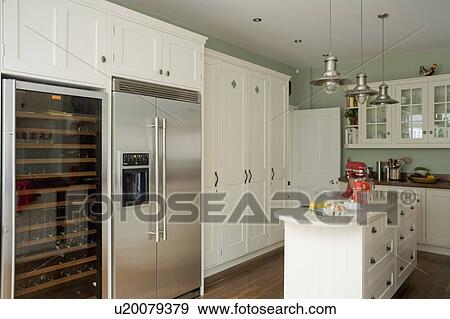 Wine cabinet and American-style fridge-freezer in kitchen with cream fitted storage cupboards and units View Large Photo Image Stock Photo - Wine cabinet and American-style fridge-freezer in kitchen with cream fitted storage cupboards and units. Fotosearch
