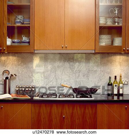 Stock Photo - Wok on hob below marble splashback and fitted wood cupboard with glazed doors. Fotosearch