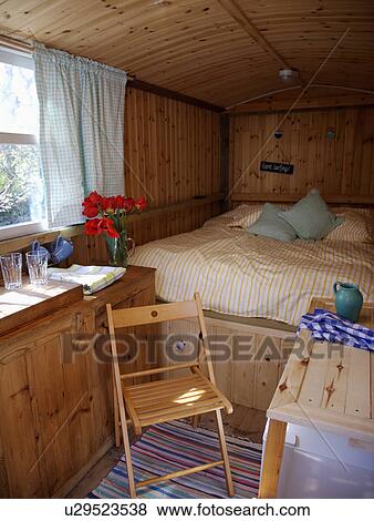 Stock Photo - Wooden chair and platform bed in garden shed used as guest bedroom. Fotosearch