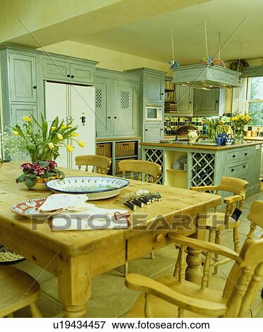 Stock Photo - Wooden chairs and table in kitchen with pastel turquoise fitted units. Fotosearch