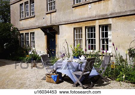 Stock Image - Wooden chairs and table with blue cloth outside old stone country house. Fotosearch