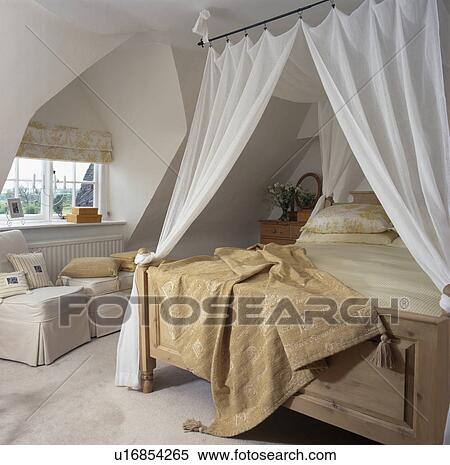 Stock Photography - Wooden chest below bed with white drapes in cream attic bedroom. Fotosearch