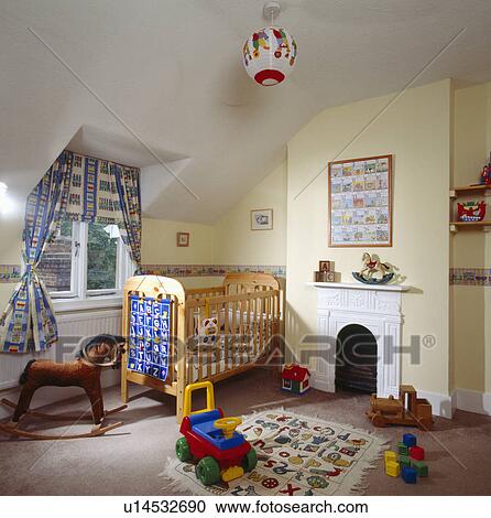 Stock Image - Wooden cot and toys on the floor of pastel yellow child's attic bedroom with small white fireplace. Fotosearch