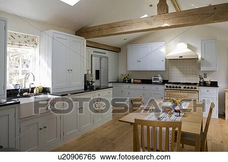 Stock Photography - Wooden table and chairs in large country kitchen with white fitted units and cupboards. Fotosearch