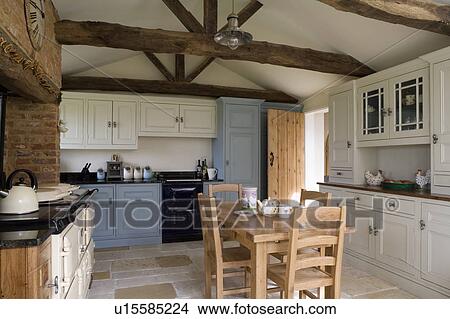 Picture - Wooden table and chairs in traditional kitchen with beamed apex roof and cream Aga. Fotosearch