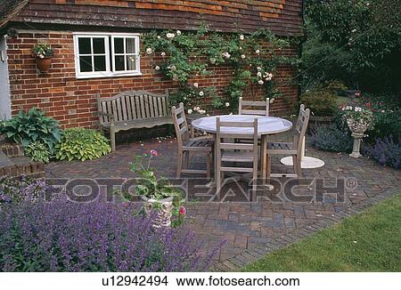 Wooden table and chairs on herringbone-brick paved patio in front of brick country cottage in summer View Large Photo Image Picture - Wooden table and chairs on herringbone-brick paved patio in front of brick country cottage in summer. Fotosearch