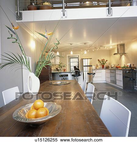 Stock Photography - Wooden table and white chairs in modern open-plan kitchen dining room. Fotosearch