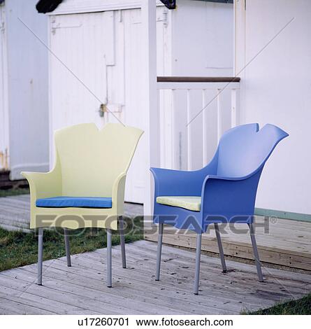 Stock Image - Yellow and blue plastic armchairs on decking in front of beach hut. Fotosearch