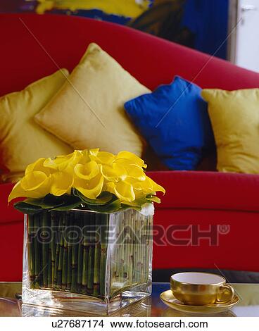 Picture - Yellow calla lilies in glass vase on table in front of red sofa with yellow cushions. Fotosearch