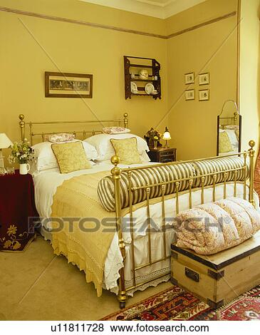 Stock Photo - Yellow throw and white linen on brass bed in yellow bedroom. Fotosearch