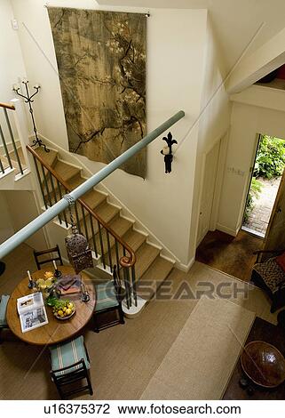 Stock Image - Aerial view of double height cream hall dining room with large tapestry on wall and antique table and chairs. Fotosearch