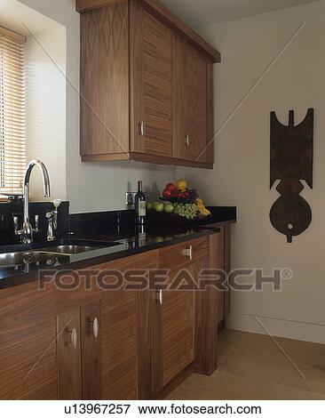 Stock Photo - African sculpture on wall of modern kitchen with black granite work top on fitted walnut units. Fotosearch
