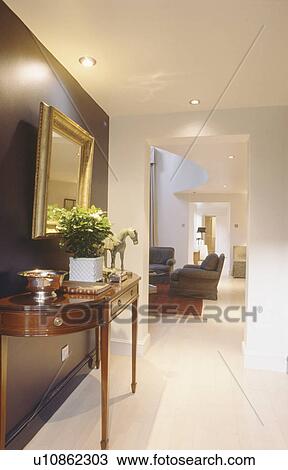 Stock Image - Antique console table against black wall of openplan eighties hall with white flooring. Fotosearch