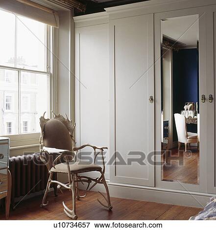 Antler chair in front of window in bedroom with grey fitted wardrobe with mirrored door View Large Photo Image Stock Photo - Antler chair in front of window in bedroom with grey fitted wardrobe with mirrored door. Fotosearch