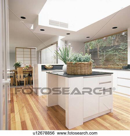 Stock Photograph - Basket of houseplants on Island unit in modern white kitchen with wooden flooring. Fotosearch
