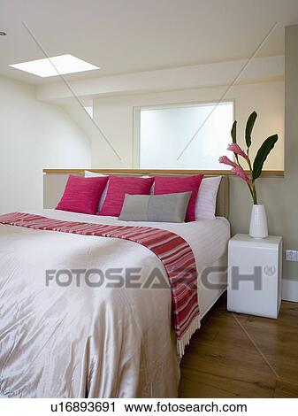Stock Image - Beige silk bedcover and pink striped throw on bed with pink and grey cushions in modern loft conversion bedroom. Fotosearch