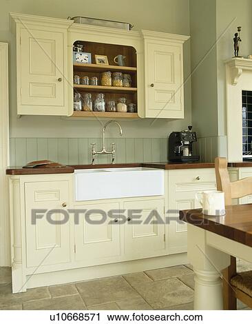 Stock Image - Belfast sink in cream fitted unit in traditional country kitchen. Fotosearch