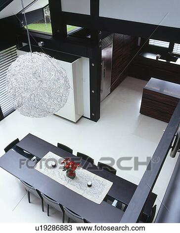 Birdseye view of circular metallic light fitting above black table and chairs in open plan dining room with white flooring View Large Photo Image Stock Image - Birdseye view of circular metallic light fitting above black table and chairs in open plan dining room with white flooring. Fotosearch
