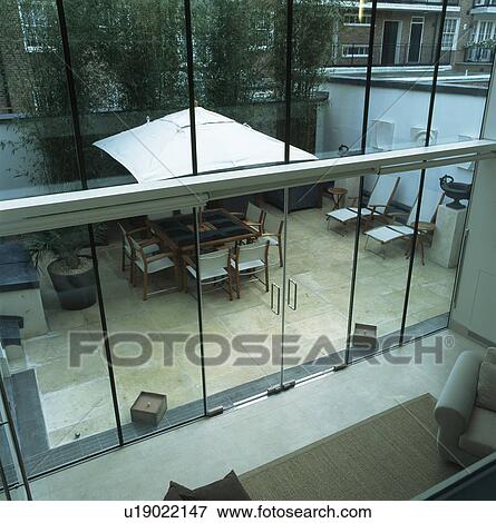 Stock Photo - Birdseye view through double-height glass wall to modern townhouse patio. Fotosearch