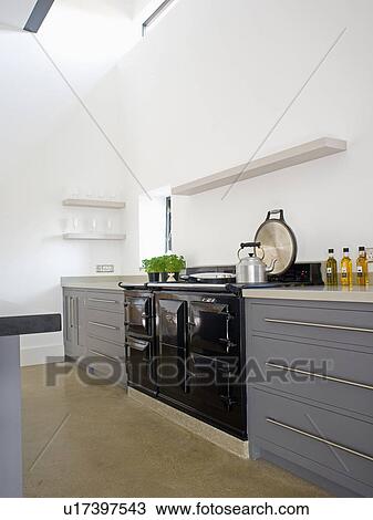 Stock Image - Black Aga oven in modern white kitchen with fitted grey units. Fotosearch