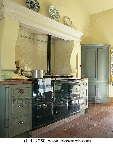 Stock Image - Black Aga oven in pastel yellow country kitchen with grey-green fitted units. Fotosearch