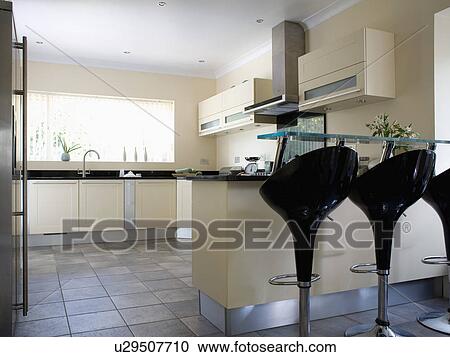 Black "Bombo" stools at breakfast bar on peninsular unit in modern cream kitchen View Large Photo Image Stock Image - Black "Bombo" stools at breakfast bar on peninsular unit in modern cream kitchen. Fotosearch