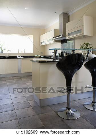 Black "Bombo" stools at breakfast bar on peninsular unit in modern cream kitchen View Large Photo Image Stock Photo - Black "Bombo" stools at breakfast bar on peninsular unit in modern cream kitchen. Fotosearch