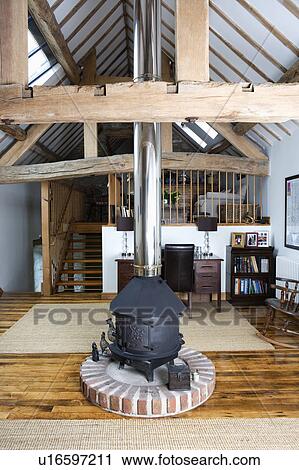 Black cast iron stove with stainless steel chimney in centre of open plan barn conversion living room with large beams View Large Photo Image Stock Image - Black cast iron stove with stainless steel chimney in centre of open plan barn conversion living room with large beams. Fotosearch