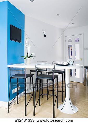 Black stools at fitted white table in modern white kitchen dining room with bright blue wall View Large Photo Image Stock Image - Black stools at fitted white table in modern white kitchen dining room with bright blue wall. Fotosearch