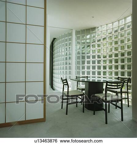 Stock Photograph - Black table and chairs in white architectural dining room with glass brick wall. Fotosearch