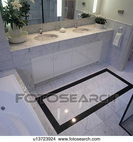 Picture - Black tiled border on marble tiled floor in modern bathroom with double inset basins. Fotosearch