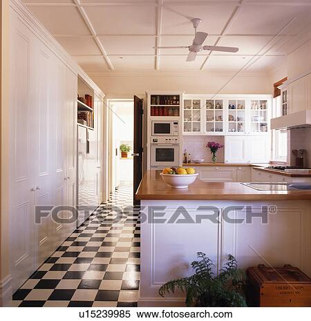 Stock Photography - Black+white chequerboard flooring in large modern white kitchen. Fotosearch