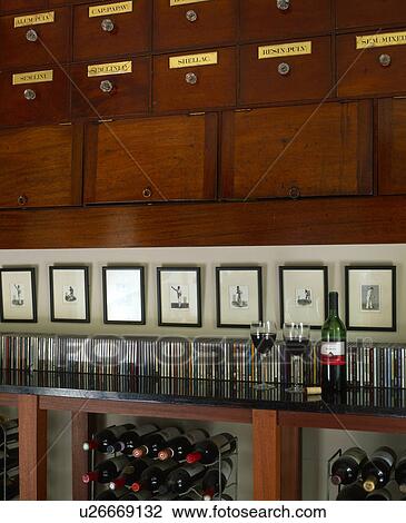 Stock Image - Black+white pictures above CDs stored on shelf above wine storage. Fotosearch