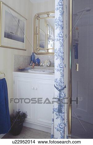 Picture - Blue and white floral curtain beside glass shower door in traditional bathroom with mirror above basin in vanity unit. Fotosearch
