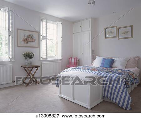 Stock Photo - Blue and white striped quilt on bed in white bedroom with white wooden chest and neutral flooring. Fotosearch