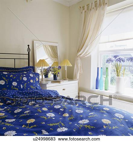 Stock Image - Blue bedlinen on bed in small bedroom. Fotosearch