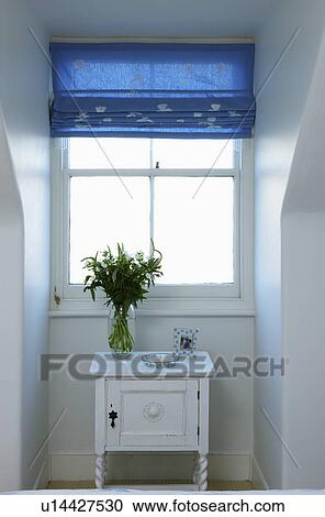Stock Image - Blue blind on window above small white painted cupboard. Fotosearch