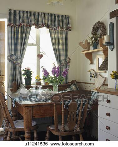 Stock Photograph - Blue checked curtains on window above wooden table and chairs in small dining room. Fotosearch