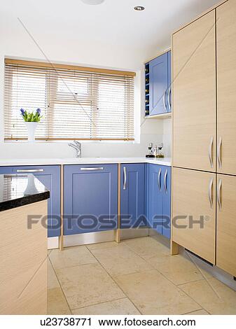 Stock Image - Blue fitted units and pale wood fitted cupboard in modern kitchen with limestone flooring. Fotosearch