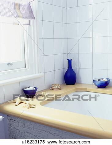 Stock Photography - Blue glass bottle and bowls on wooden bath surround in white tiled bathroom. Fotosearch